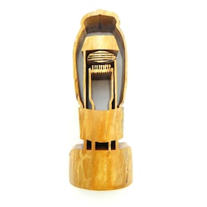 May include: A wooden sculpture of a lamp, cut in half to show the inner workings. The lamp is made of light brown wood and has a round base.