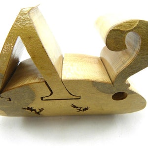 May include: A wooden puzzle in the shape of a question mark. The puzzle is made of multiple pieces that fit together to form the shape. The puzzle is made of light brown wood and has a natural finish.