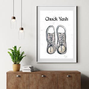 May include: A framed print featuring a watercolor illustration of two Converse sneakers with laces tied. The text "Chuck Yeah" is above the sneakers. The sneakers are gray with white laces and soles.