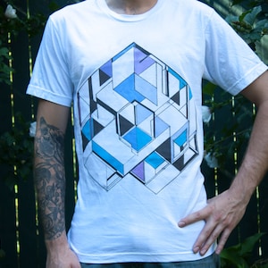 以下が含まれることがあります： 黒、青、紫の幾何学模様がプリントされた白いTシャツ。デザインは、重なり合った正方形と長方形の複雑なパターンです。