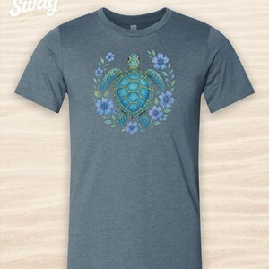 Puede incluir: Camiseta azul con un dise&ntilde;o de tortuga marina turquesa rodeada de flores azules. La tortuga tiene un contorno dorado y est&aacute; centrada. El texto "CSS Swag" est&aacute; en la esquina superior izquierda.