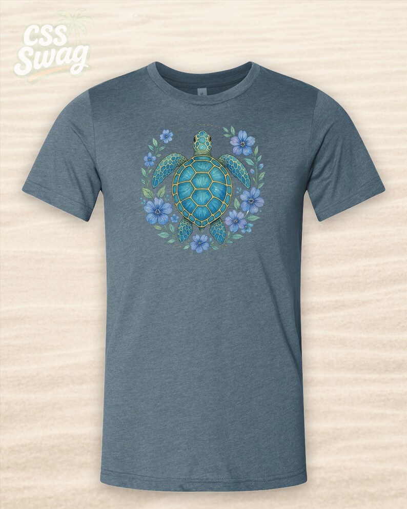 Puede incluir: Camiseta azul con un dise&ntilde;o de tortuga marina turquesa rodeada de flores azules. La tortuga tiene un contorno dorado y est&aacute; centrada. El texto "CSS Swag" est&aacute; en la esquina superior izquierda.