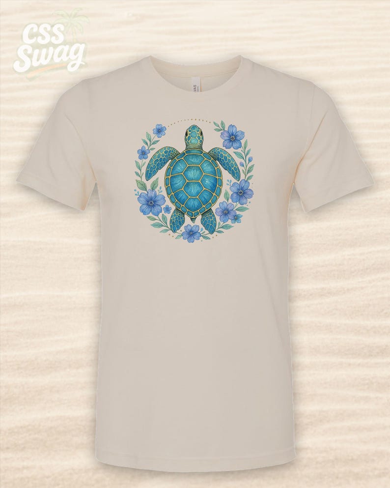 Puede incluir: Camiseta color crema con un dise&ntilde;o detallado de tortuga marina turquesa rodeada de flores azules y hojas verdes. La tortuga tiene un caparaz&oacute;n estampado. La camiseta tiene mangas cortas y cuello redondo.