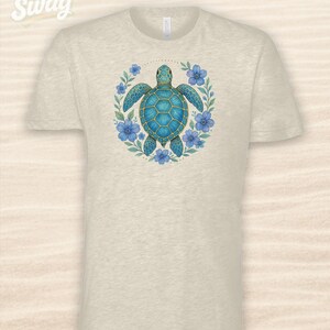 Puede incluir: Camiseta beige con una ilustraci&oacute;n detallada de una tortuga marina turquesa rodeada de flores azules y hojas verdes. El dise&ntilde;o est&aacute; centrado en la camiseta. El texto "CSS Swag" est&aacute; en la esquina superior izquierda.