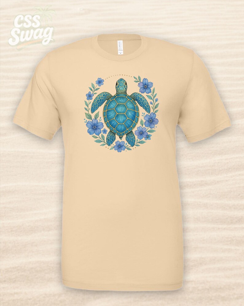 Puede incluir: Una camiseta beige con un dise&ntilde;o de tortuga marina azul rodeada de flores azules y hojas verdes. La camiseta tiene el texto "CSS Swag" en la esquina superior izquierda.