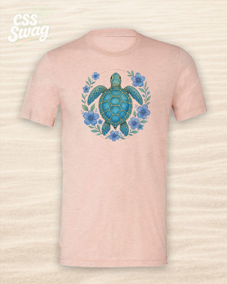 Puede incluir: Camiseta rosa claro con un dise&ntilde;o de tortuga marina turquesa rodeada de flores azules y hojas verdes. El texto "CSS Swag" es visible en la parte superior izquierda. Cuello redondo.