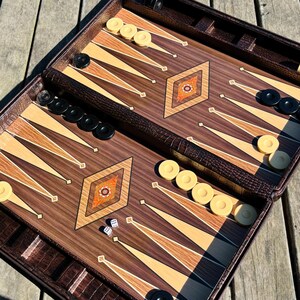 a backgammon game board with pieces and a leather case, placed on a wooden surface.