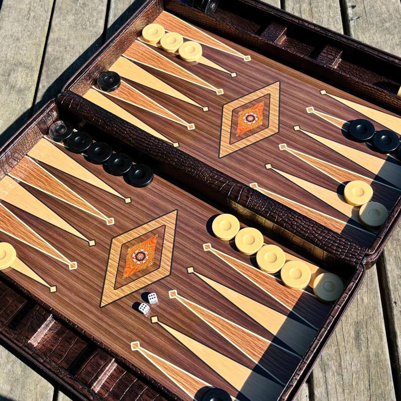a backgammon game board with pieces and a leather case, placed on a wooden surface.