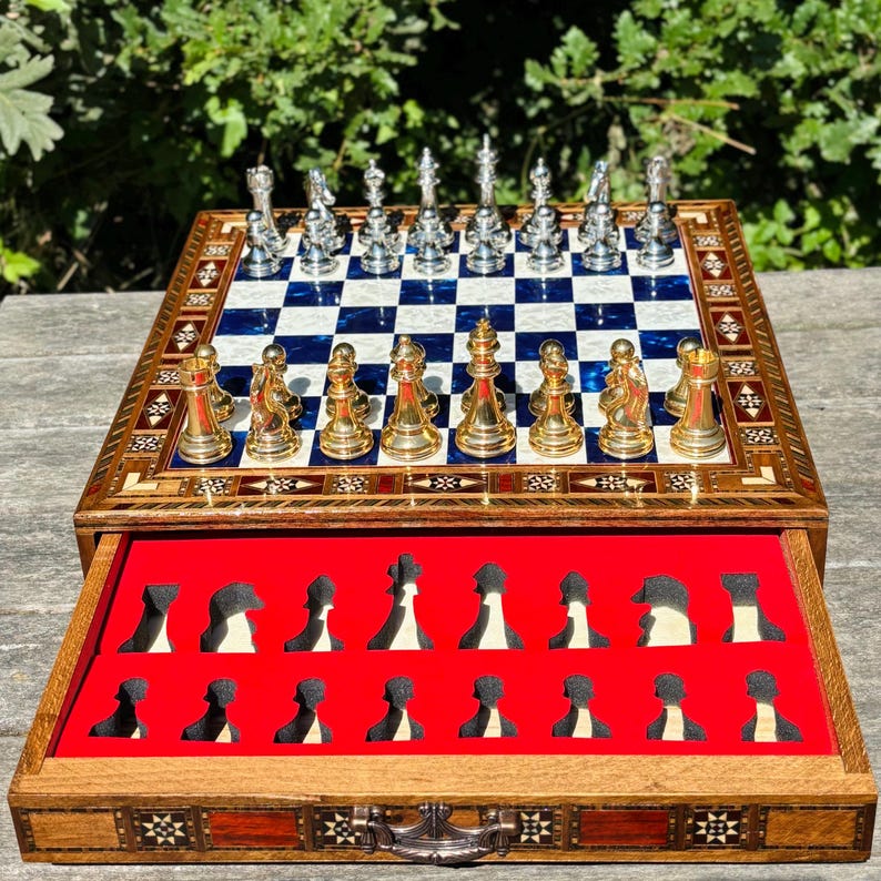 A chess set with a wooden frame and a blue and white checkered board, with the pieces inside a red drawer.