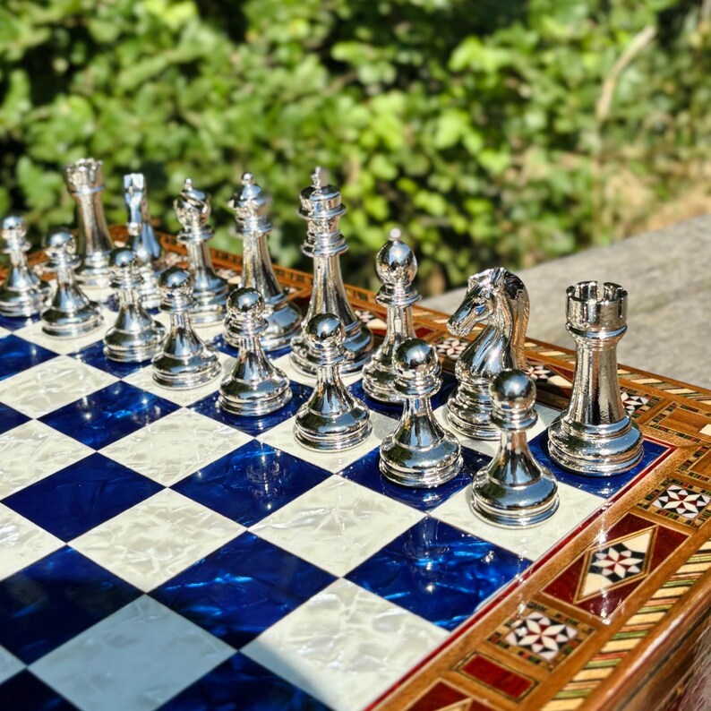A chess set with a blue and white checkered board, featuring a variety of chess pieces including the king, queen, and other pieces, arranged on the board.