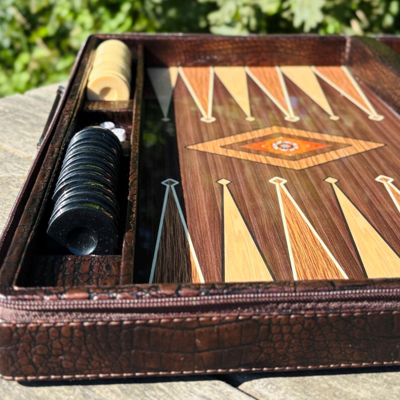 A wooden backgammon board with a decorative pattern and a set of playing pieces, including a set of dice, placed on a wooden surface.