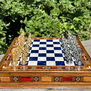 A chess set with a blue and white checkered board and pieces, including white and gold pieces, placed on a wooden board with decorative patterns.