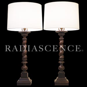 May include: Two matching table lamps with white drum shades. The dark brown bases have a carved, twisted design. The lamps are on a black background. The text "RADIASCENCE" is displayed in white.
