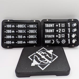 May include: Two black rectangular game trackers with white numerical and icon labels, including values from -100 to +800, and text like TAUNT, STEALTH, and NIGHT. A separate black rectangular cover features a white circular graphic design.