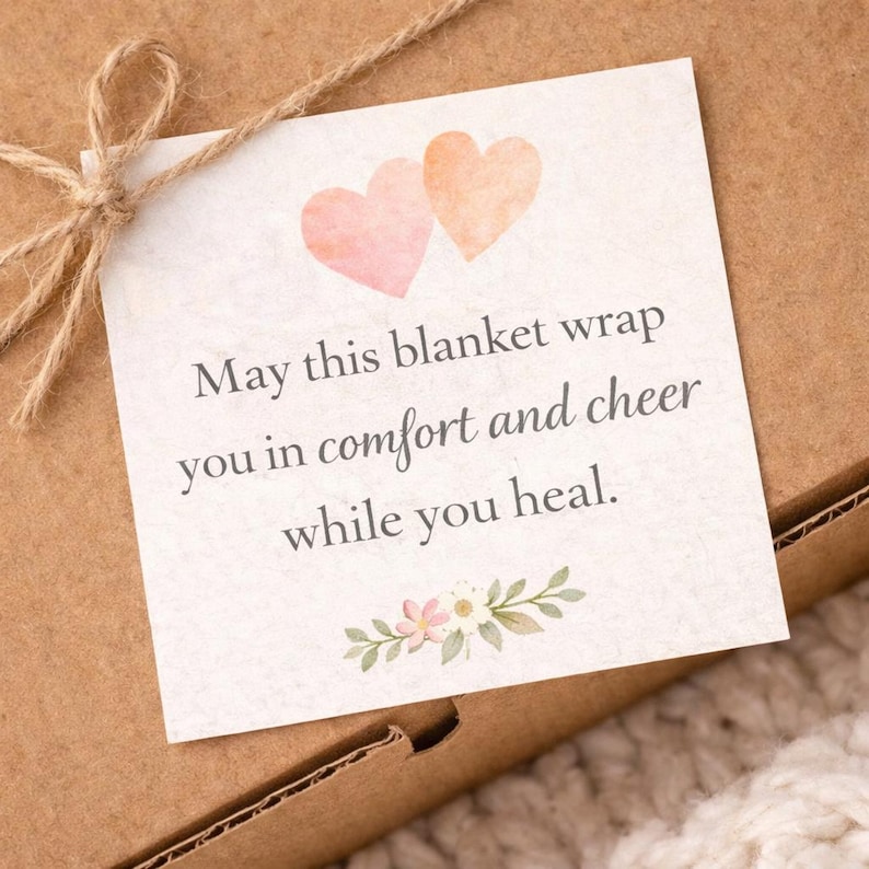 Puede incluir: Una tarjeta cuadrada con el texto "May this blanket wrap you in comfort and cheer while you heal" est&aacute; atada a una caja de cart&oacute;n marr&oacute;n con hilo. La tarjeta tiene dos corazones de acuarela y detalles florales.