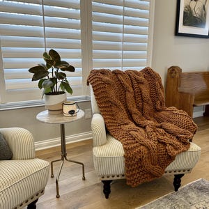 Luxury chunky knit blanket styled in a warm neutral living room, timeless new homeowner gift for sofa, chair, or bedroom. Rust knitted blanket