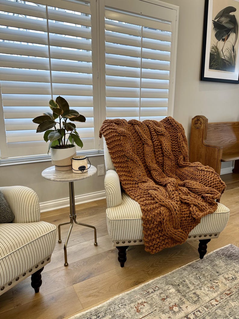 Luxury chunky knit blanket styled in a warm neutral living room, timeless new homeowner gift for sofa, chair, or bedroom. Rust knitted blanket