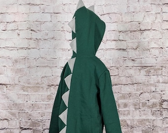 May include: A green hooded sweatshirt with gray triangular accents resembling a dinosaur. The sweatshirt has a zipper closure and ribbed cuffs and hem. The hood features gray spikes.