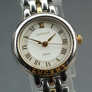 May include: A Seiko Lucent wristwatch with a silver and gold-tone band and case. The watch face is white with black Roman numerals and gold hands. The word "LUCENT" is printed on the watch face and band.