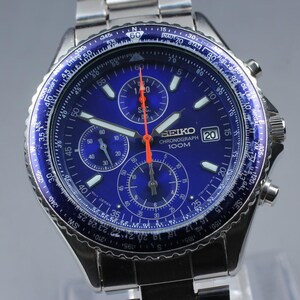 May include: A stainless steel Seiko Chronograph watch with a blue dial and bezel. The watch features multiple sub-dials, luminous hands, and a date display at the 3 o'clock position. The watch is water-resistant to 100 meters.