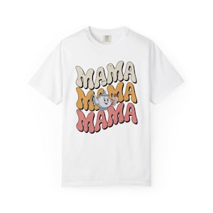 May include: White t-shirt with the word "MAMA" in a retro font, stacked three times. The middle "MAMA" features a teapot and a pig illustration. The text is in cream, orange, and pink.