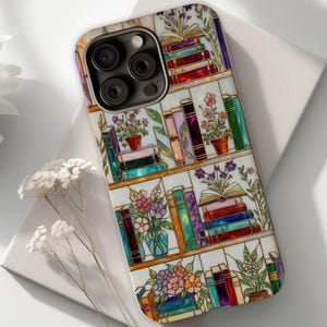 May include: A phone case featuring a colorful stained-glass design of a bookshelf. The design includes stacks of books, potted flowers, and open books. The case has a glossy finish and a multi-camera lens cutout.