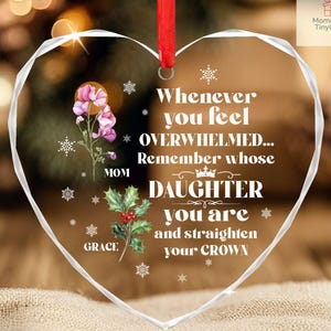 May include: A heart-shaped glass ornament with a red ribbon for hanging. The ornament features the text "Whenever you feel OVERWHELMED... Remember whose DAUGHTER you are and straighten your CROWN." Floral and snowflake designs are also included.