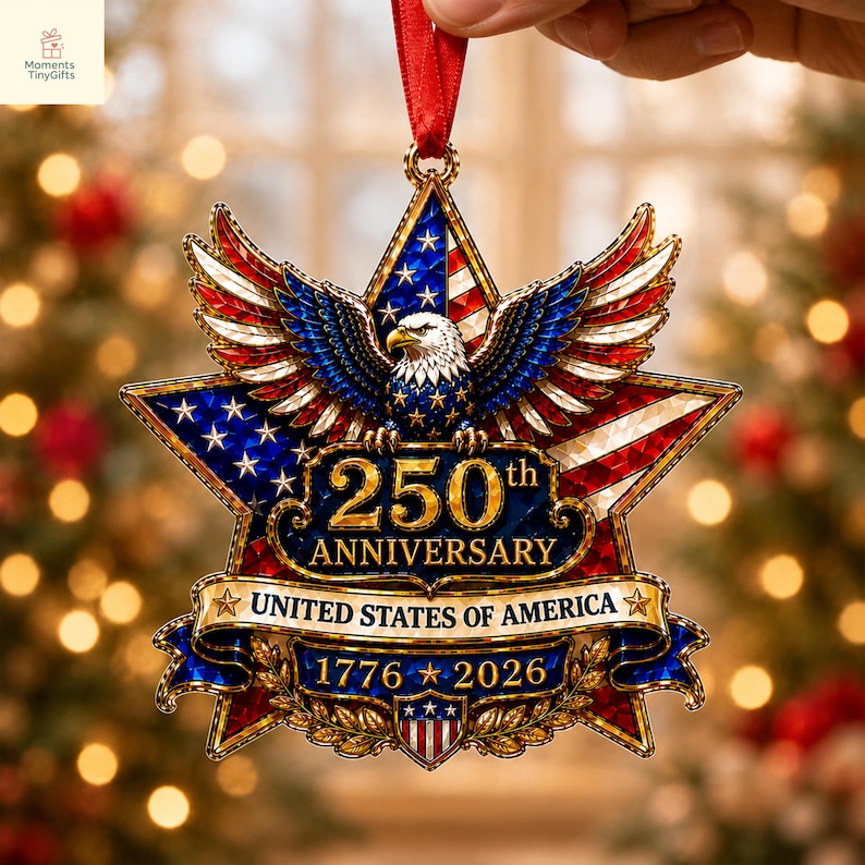 May include: A star-shaped hanging ornament featuring a bald eagle with spread wings, the American flag, and gold text reading 250th ANNIVERSARY UNITED STATES OF AMERICA 1776-2026. The design includes a red ribbon hanger and a small shield at the base.