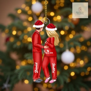 May include: A Christmas tree ornament featuring a couple in red pajamas and Santa hats. The woman is pregnant, with the text "Baby 2026" on her pajamas. The man's pajamas say "David," and the woman's say "Stella."