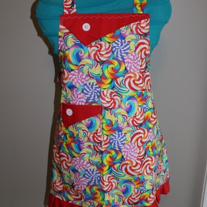 May include: A red and white apron with a colorful lollipop print. The apron has two pockets and a ruffled hem.