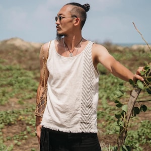 Puede incluir: Camiseta sin mangas color crema con un diseño de chevron texturizado en la parte delantera. La camiseta sin mangas tiene un dobladillo deshilachado y se usa con pantalones negros. La imagen está tomada al aire libre en un día soleado.