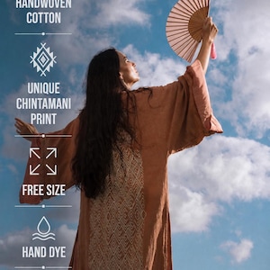 a woman wearing a brown robe and holding a fan, with a blue sky and clouds in the background.