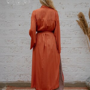 May include: A rust-coloured, long-sleeved dress with a matching belt, paired with loose grey trousers. The dress features a button-down design and a side slit. The brand name "chintamani" is visible in the upper left corner.