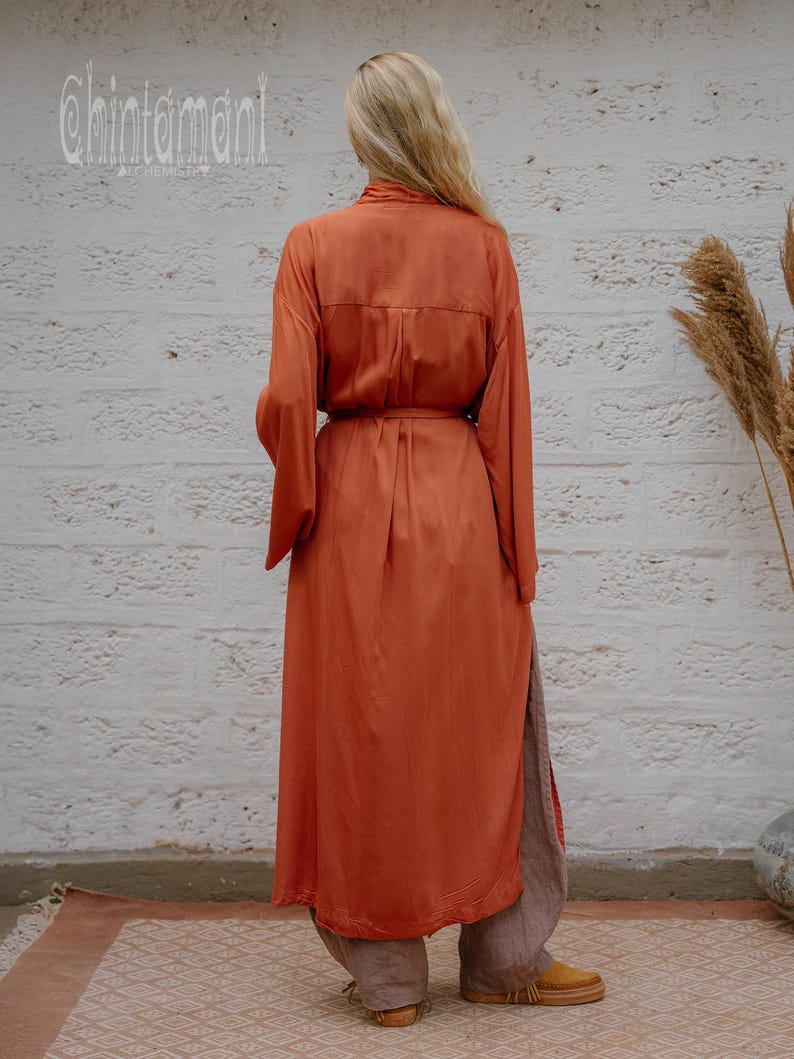 May include: A rust-coloured, long-sleeved dress with a matching belt, paired with loose grey trousers. The dress features a button-down design and a side slit. The brand name "chintamani" is visible in the upper left corner.
