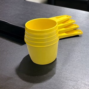 May include: Four yellow plastic measuring cups stacked on top of each other. The cups have handles and are designed for measuring dry or liquid ingredients.