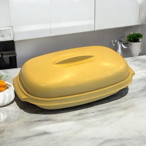 May include: A yellow ceramic baking dish with a lid. The dish has a rounded oval shape and a smooth, glossy finish.