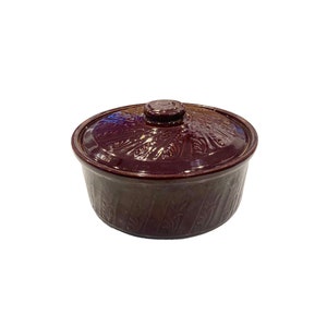May include: A brown ceramic casserole dish with a lid. The dish has a decorative pattern of leaves and swirls.