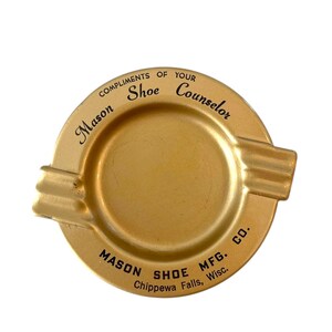 May include: A vintage gold-colored ashtray with the text "COMPLIMENTS OF YOUR Mason Shoe Counselor" and "MASON SHOE MFG. Chippewa Falls, Wisc. CO." The ashtray has two rests and a circular center.