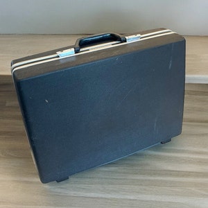 May include: A black hard-sided suitcase with a silver handle and clasps.
