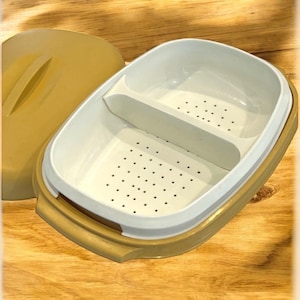 May include: A beige plastic food container with a lid. The container has two compartments, one with a strainer and the other without. The container is ideal for storing and serving food.