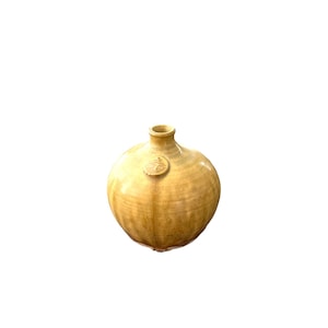 May include: A small, round, yellow ceramic vase with a slightly flared opening. The vase has a subtle glaze and a textured surface.