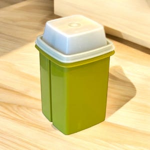 May include: A green rectangular container with a white lid. The container is made of plastic and has a square shape. The lid has a small circular indentation in the center. The container is sitting on a wooden surface.