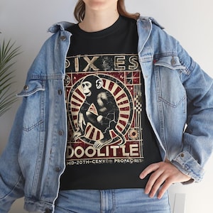 May include: Black t-shirt with a distressed graphic of a monkey in a circular design. The text "PIXIES" is above the monkey, and "DOOLITTLE" is below. Additional text reads "MID-20TH-CENTURY PROPAORES".