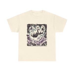 May include: Cream-colored t-shirt featuring a graphic illustration of a person floating in the air, with feet pointing upwards. The graphic is in shades of black, purple, and white, with the text "WITH YOUR FEET IN THE AIR AND YOUR HEAD ON THE GROUND".