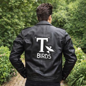 May include: Black leather jacket with the text "T BIRDS" in white lettering and a white bird graphic on the back. The jacket has a classic biker style with a notched collar and a zipper closure.