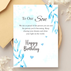 May include: A birthday card with the message "To Our Son" in elegant script. The card features blue watercolor floral accents and the words "Happy Birthday". The card is on a wooden tray with a beige envelope.