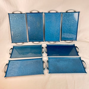 May include: Eight blue metal serving trays with silver handles. The trays are rectangular and have a textured surface.