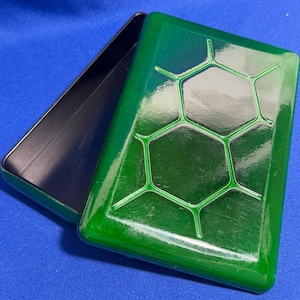 May include: A rectangular, open box with a glossy green lid featuring a honeycomb design. The lid is slightly ajar, revealing the black interior of the box. The box is set against a blue background.