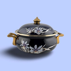 May include: A dark navy blue lidded casserole dish featuring hand-painted light purple and white orchid floral motifs. The pot includes two gold-toned side handles and a matching gold-toned knob on the lid, with a metallic rim around the edge.