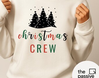 May include: Cream-colored sweatshirt with a black Christmas tree graphic and the words "christmas CREW" in red and green. The design includes black dots above the trees. A festive holiday-themed apparel item.